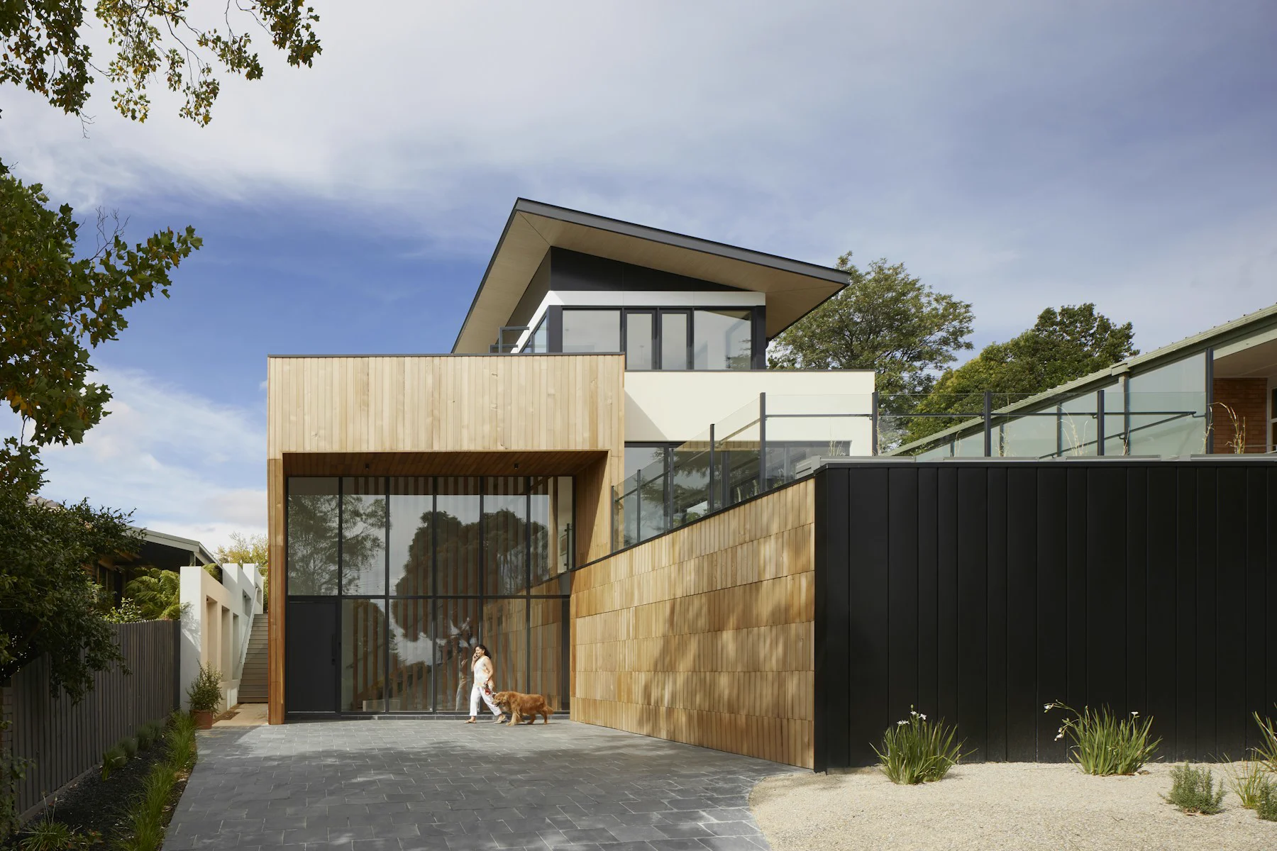 Fachada de una vivienda contemporánea con revestimiento de madera, grandes ventanales y acceso pavimentado